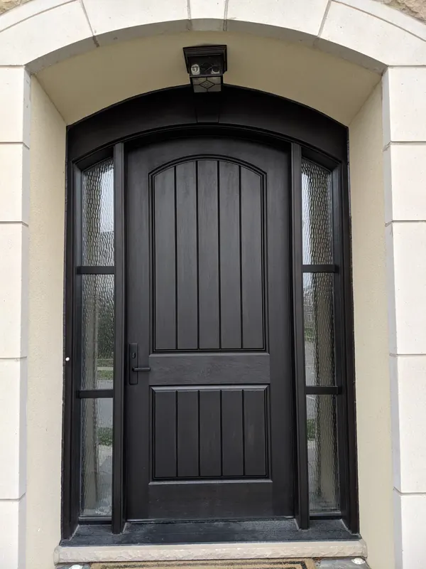 Dark fiberglass entry door with arched top and textured glass sidelites in a stone surround