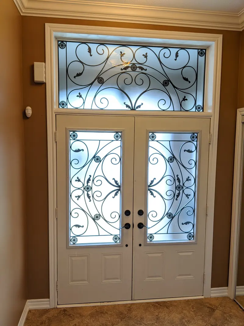 Double entry doors with wrought-iron glass and a matching transom