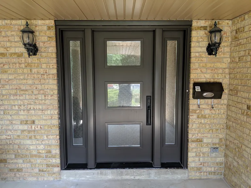 Modern black fiberglass entry door with three glass lites and tall sidelites between lanterns