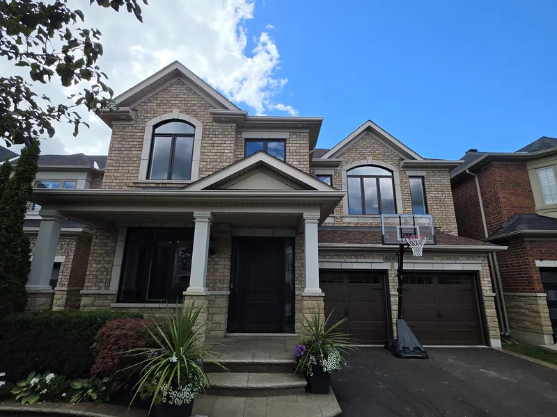 Tan brick two-storey home with arched black-framed windows, a covered porch and a double garage