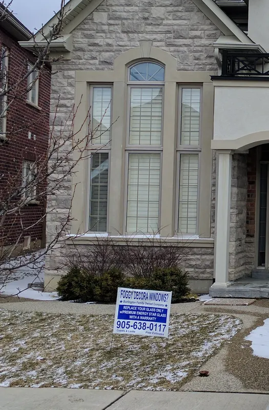 Stone and stucco home with a lawn sign reading Foggy Decora Windows? Replace your glass only, with the phone number 905-638-0117